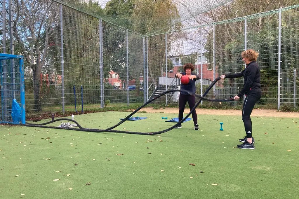 Personal training met battle ropes op een omheind sportveld
